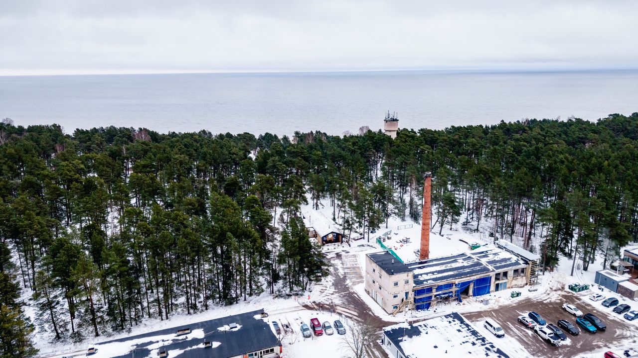 Aerial winter view of a snowy forest with an industrial area by the Baltic Sea in Ķesterciems, Latvia.