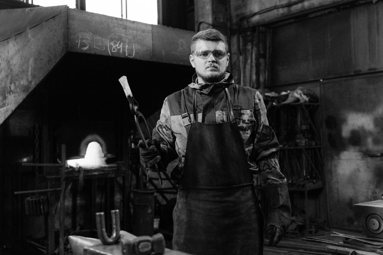 Experienced blacksmith with wolf jaw tongs in an industrial workshop setting.